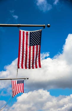 2 United States flags with a blue sky and clouds in the background